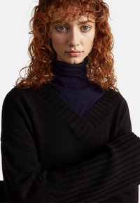 Czarny sweter dzianinowy z dekoltem w kształcie V, z prążkowanymi detalami na kołnierzu i rękawach, zestawiony z dopasowanym granatowym golfem pod spodem.