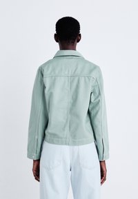 Miętowa dżinsowa kurtka z wyraźnym kołnierzem, długimi rękawami i widocznymi szwami; noszona z jasnoniebieskimi dżinsami.