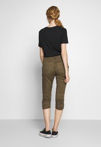 Černé tričko s krátkým rukávem spárované s olivově zelenými zkrácenými kalhotami. Kalhoty mají detail nabraných nohavic a zadní kapsy s jemným prošíváním.