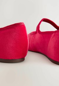Punaiset samettipolviset ballerinat, joissa on matala korko, pyöristetty kärki ja kangasremmi. Pintamateriaali on sileä, saumaton muotoilu ja hienovarainen tekstuuri.