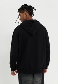 Zwarte hoodie met een trekkoord in de capuchon, geribbelde manchetten en zoom. Sweatshirtstijl met een ontspannen pasvorm en zachte textuur. Duidelijke stikseldetails.