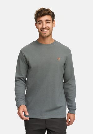 Sudadera de manga larga y cuello redondo en un color verde apagado, con un diseño de textura acanalada y un pequeño logo redondo en el pecho.
