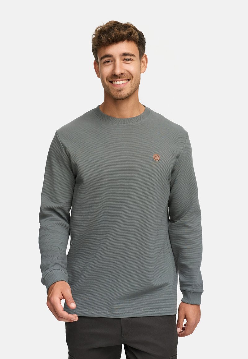Langärmliger Sweatshirt mit Rundhalsausschnitt in einem gedämpften Grünton, der über ein strukturiertes Rippdesign und ein kleines runde Logo auf der Brust verfügt.
