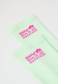 Mintgroene enkelkousen hebben een levendige roze print van "BMW BERLIN MARATHON" en een afbeelding van de Brandenburger Tor.