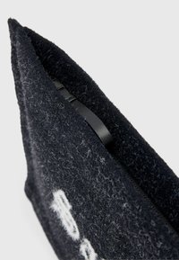 Pogled od blizu na tamni krzneni materijal s vrećom s bijelim izvezenim uzorkom i crnim patentnim zatvaračem djelomično vidljivim unutra.