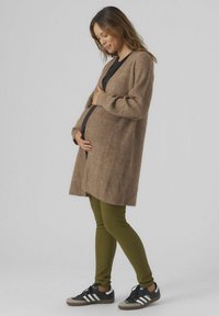 Cardigan en tricot marron avec des manches longues, une ouverture sur le devant et une finition texturée, associé à des leggings côtelés verts olive et des baskets noires.