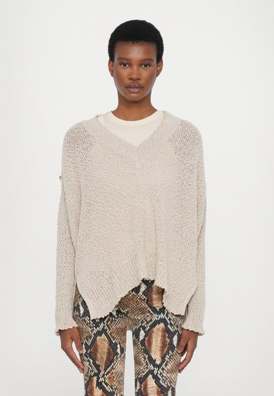 Suéter de punto beige con escote en V, corte holgado y dobladillo deshilachado. Combinado con leggings de estampado de serpiente que presentan patrones en marrón y negro.