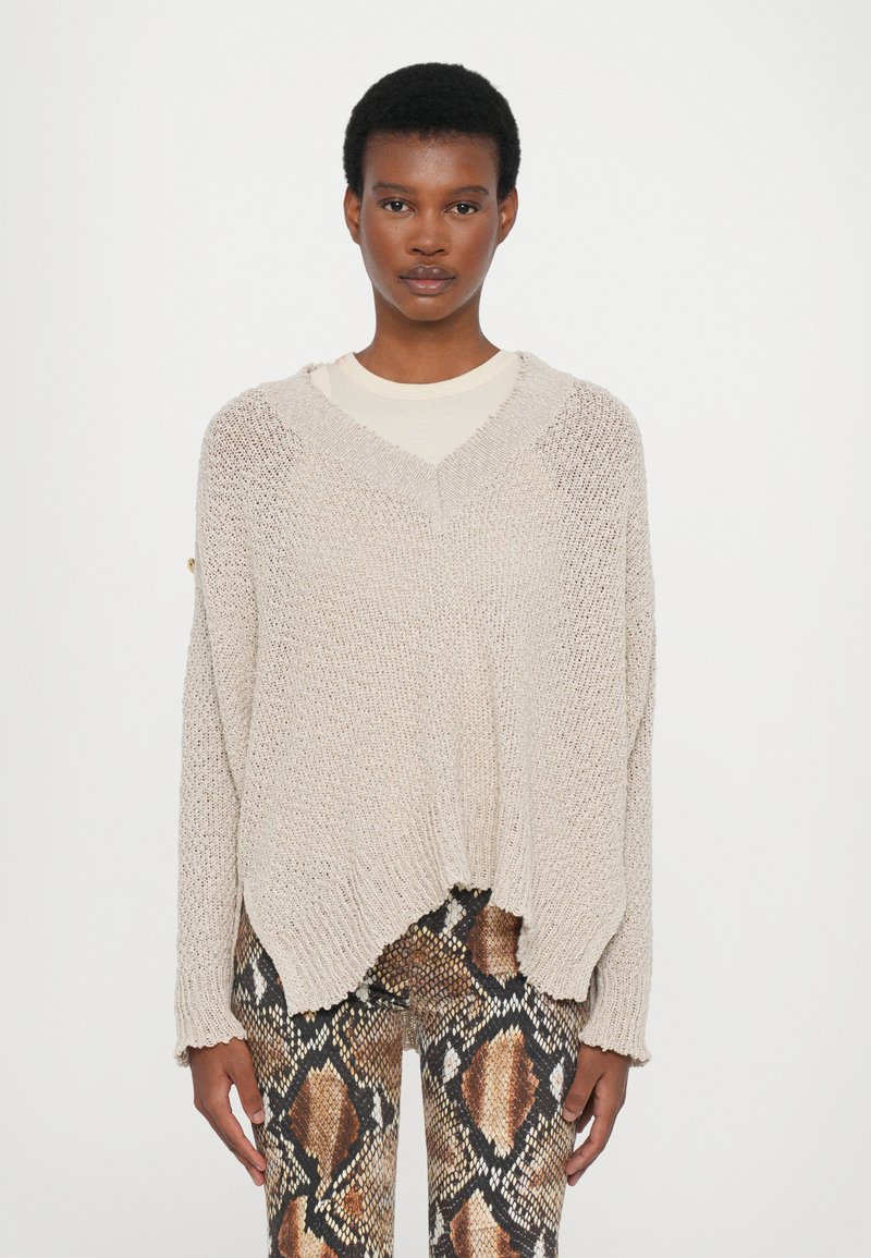 Beige knitted pullover with a V-neckline, loose fit, and frayed hem. Paired with snake-print leggings featuring brown and black patterns.