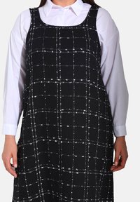 Robe à carreaux noir et blanc avec un design sans manches, fabriquée en tissu texturé, dotée d'un décolleté carré et d'une coupe ample.