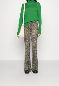 Maglione verde lavorato a maglia con collo alto, abbinato a pantaloni svasati a fantasia nei colori blu, giallo e marrone. Borsa bianca e scarpe nere.