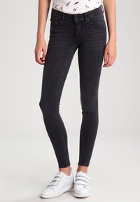 Jeans ajustados negros con una textura suave y una cintura de altura media. Combinados con zapatillas blancas con tiras de velcro.
