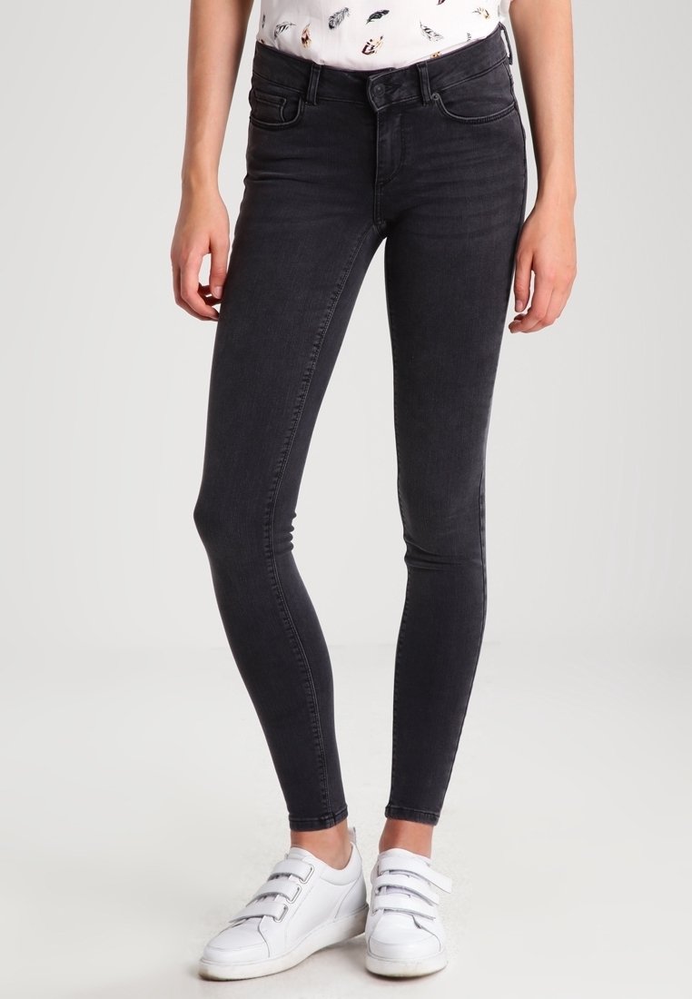 Jeans ajustados negros con una textura suave y una cintura de altura media. Combinados con zapatillas blancas con tiras de velcro.