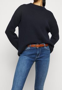 Marinblå stickad tröja med rundad halsringning och långa ärmar, kombinerad med åtsittande ljusblå jeans och ett brunt läderbälte.