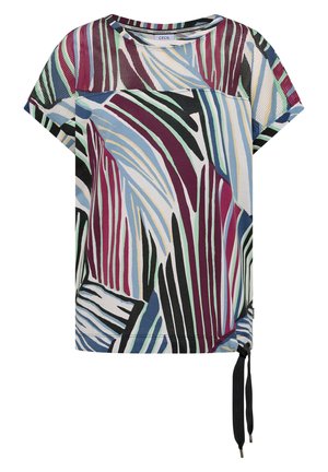 Femme de dos portant un haut à manches courtes avec un motif rayé abstrait dans des tons bleu, noir, bordeaux, blanc et vert sur fond blanc.