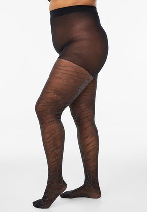 Kurvige Person, die schwarze, durchscheinende Strumpfhosen mit einem dezenten schimmernden Zebramuster trägt und vor weißem Hintergrund steht.