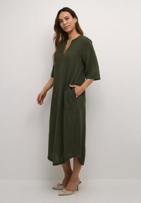 Vestido de lino verde oliva con escote en V, mangas cortas y bolsillos laterales; presenta un ajuste relajado y longitud a media pantorrilla.