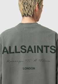 Olivgrön sweatshirt med stora mörkgröna bokstäver "ALLSAINTS" och "Message To A Father" på baksidan, tillverkad av mjukt material.