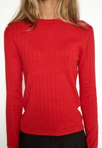 Suéter rojo de punto con mangas largas, textura acanalada y pequeños agujeros, con cuello redondo y cintura ceñida.
