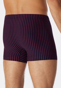 Boxer di colore blu navy scuro con sottili strisce rosse, una comoda cintura elastica e una vestibilità aderente intorno alle gambe.