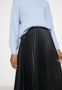 Světle modrý pletený svetr s ribbovanou texturou, spojený s černou skládací sukní z lesklého materiálu s vertikálními sklady.
