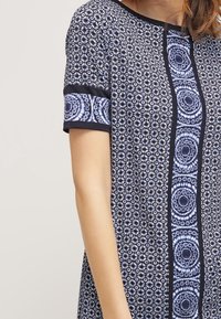 Marinblå klänning med blommönster och cirkulära mönster, korta ärmar med kontrasterande svart kant, slät textur, kn älång design.