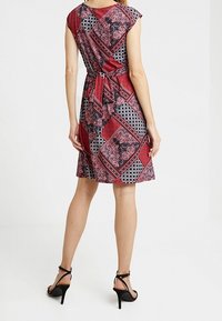 Rotes und schwarzes gemustertes Kleid mit kurzen Ärmeln, Taillengürtel und schwingendem Rock. Glattes Material mit floralen und geometrischen Designs. Hohe Absätze.