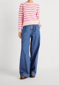Gestreepte roze en witte gebreide trui met een geribde onderkant, gecombineerd met losse blauwe denim trousers. Kenmerken zijn wijde benen en een elastische tailleband.