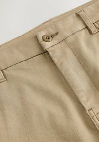 Khaki trousers featuring a smooth fabric with a fine diagonal texture, a front button closure, and reinforced stitching on the waistband.