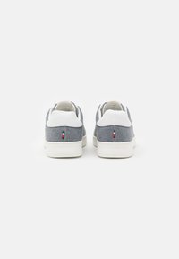 Un paio di sneakers basse grigie e bianche viste da dietro, con suole bianche e un piccolo dettaglio di bandiera rossa, bianca e blu su ogni tacco.