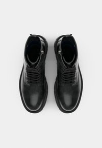 Stivali alla caviglia in pelle nera con finitura testurizzata, punta rotonda, allacciatura frontale e zipper laterale. Presentano una suola in gomma robusta e un interno imbottito.