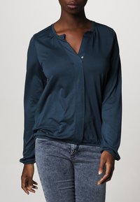 Dunkelblau-grünes Button-Up-Hemd mit V-Ausschnitt, langen Ärmeln, gerafftem Kragen und elastischen Bündchen. Weicher Stoff mit glatter Textur.