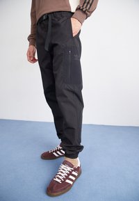 Svarta tapered joggers i lättviktsmaterial, med en ficka med dragkedja på sidan och ett elastiskt midjeband med snörning.