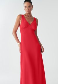 Punane varrukateta maksikleit V-kaelusega. Sile ja voolav kangas, lõdvestunud lõikega ning diskreetse kogumisega rinna juures.