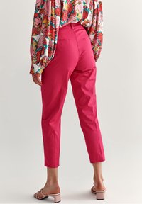 Pantalons coupés roses vifs avec une taille ajustée et des poches latérales, associés à un chemisier à motifs floraux. Tissu en coton lisse.