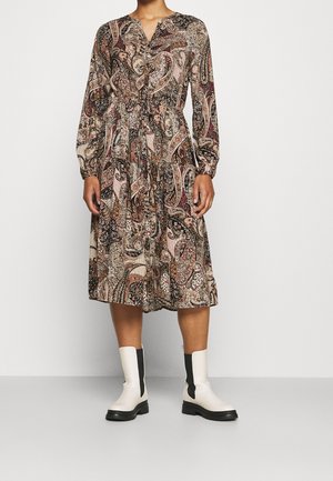 Kvinde iført en flerfarvet paisley midi-kjole med lange ærmer, kombineret med hvide ankelstøvler med sorte elastiske sidepaneler.