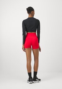 Crni dugi rukavi crop top s bijelim prugama, uparen s crvenim šortsevima visokog struka. Model nosi crne teniske cipele i tamne čarape.