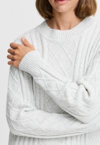 Weißer Strickpullover mit strukturiertem Oberflächen, geripptem Halsausschnitt und Bündchen. Verfügt über Rautenmuster und eine entspannte Passform.