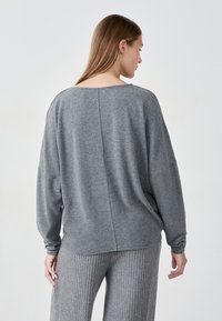 Grauer Pullover mit lockerer Passform, weitem Ausschnitt und langen Ärmeln. Weicher Stoff und Nahtdetails auf der Rückseite. Kombiniert mit passenden Ripp-Hosen.