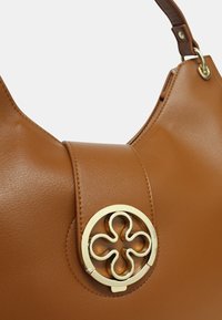 Bruine leren handtas met een ronde vorm en een metalen logo-accent op de voorkant. Glad textuur met een brede schouderband.