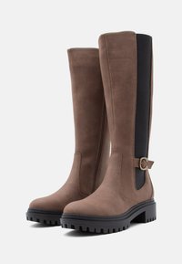 Braune knöchelhohe Stiefel aus weichem Wildleder mit einem schwarzen elastischen Einsatz, einem metallischen Akzent an der Seite und einer strukturierten Gummisohle.