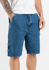 Shorts de mezclilla en un tono azul medio, con un corte holgado, cintura con botón, bolsillos laterales y dobladillo costurado.