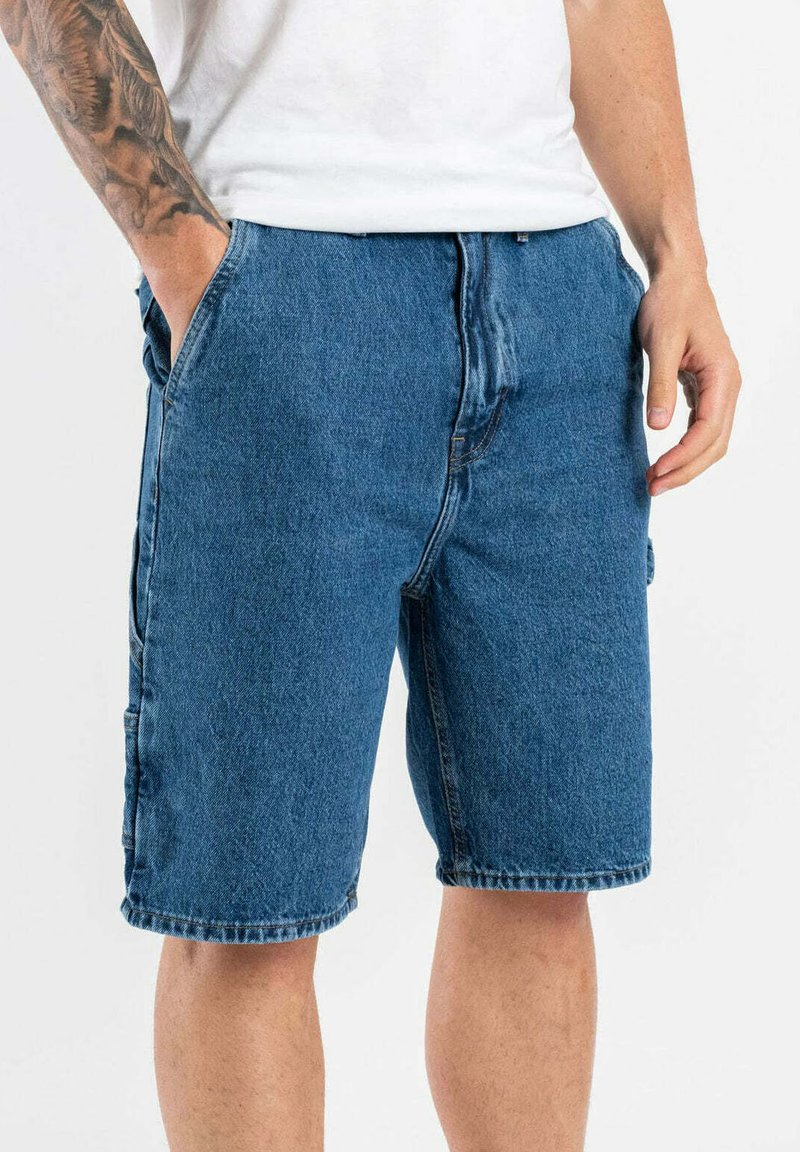 Shorts de mezclilla en un tono azul medio, con un corte holgado, cintura con botón, bolsillos laterales y dobladillo costurado.