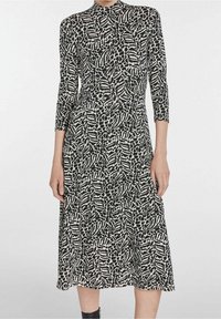 Czarna i biała sukienka w wzory z wysokim dekoltem, rękawami o długości trzech ćwierci oraz swobodnym krojem sięgającym do połowy łydki. Miękka tekstura materiału.