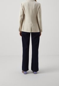 Beige striped blazer with a fitted shape, vent detail at the back, paired with navy wide-leg pants and purple block-heeled shoes.