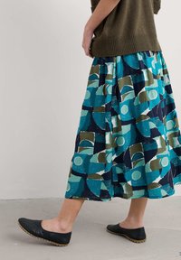 Hosszú, mintázott szoknya tengeri zöld, kék és zöld árnyalatokban, geometriai formákkal. Fekete, lapos, slip-on cipőkkel párosítva.