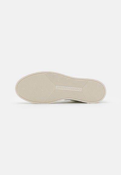 Sole of a shoe in light beige rubber with a textured pattern, featuring horizontal and diagonal grooves for grip.