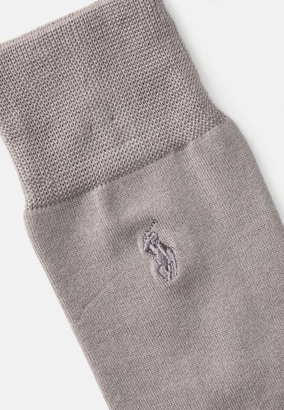 Calcetín gris hecho de tela de punto. Presenta un borde acanalado y un sutil logotipo bordado en el costado. Textura suave y color uniforme.