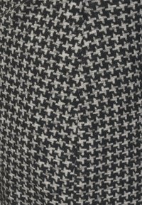 Schwarz-weißer Hahnentrittmusterstoff mit weicher Textur, der ein deutliches gewebtes Design und abwechselnde Formen in einer kompakten Anordnung aufweist.