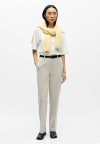 Svijetlosivi krojeni hlače s crnim remenom, uparene s bijelom majicom i žutom teksturiranom maramom koja je prebačena preko ramena. Crne cipele.