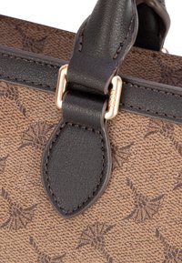 Bolsa de tela marrón con textura y acentos de cuero oscuro, con herrajes dorados y un patrón de diseños pequeños e intrincados.